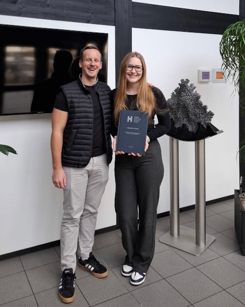 Ein Mann und eine Frau präsentieren stolz einen Preis und lächeln in die Kamera.