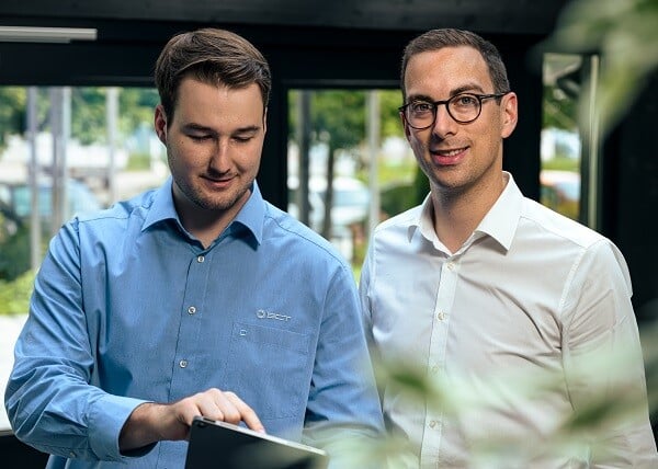 Zwei Männer in Hemden und Brillen schauen auf einen Laptop.